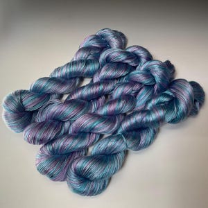 May include: Several skeins of hand-dyed yarn in shades of blue, teal, and purple. The yarn is twisted into neat bundles, showcasing the color variations. The yarn has a subtle sheen, suggesting a soft, luxurious fiber.