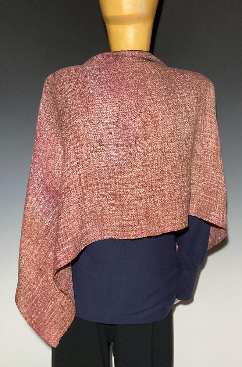 May include: A textured, woven shawl in a muted dusty rose color with a visible herringbone pattern. The shawl is draped over a dark navy blue long-sleeved shirt and black trousers, displayed on a mannequin torso against a neutral background.