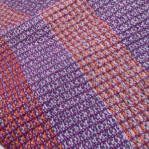 May include: Close-up of a woven fabric with a diagonal pattern in shades of purple, orange, and white.