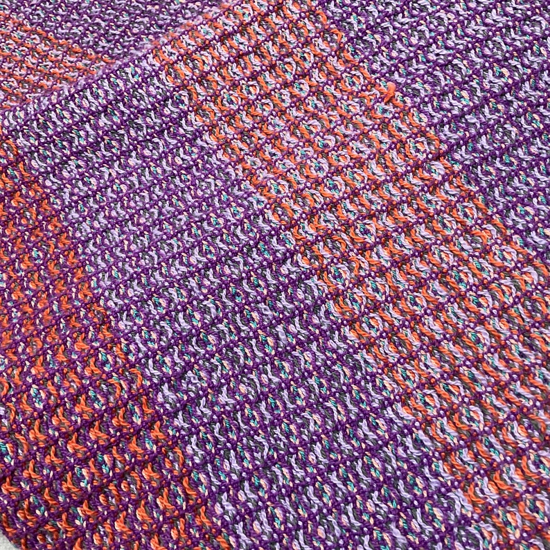 May include: Close-up of a woven fabric with a diagonal pattern in shades of purple, orange, and white.