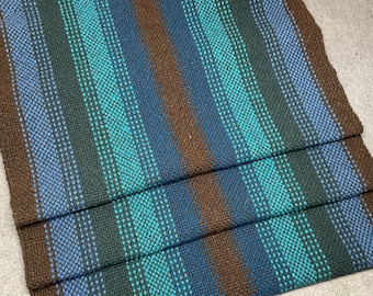 May include: A stack of woven fabric in brown, blue, and teal stripes. The fabric is folded in thirds, showing the pattern on all sides.