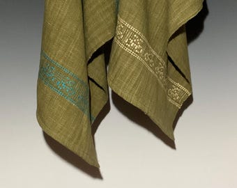 May include: Olive green linen fabric with decorative embroidered borders. One border features a turquoise geometric pattern, while the other has a cream-colored, detailed design. The fabric is draped, showcasing its texture and color variations.