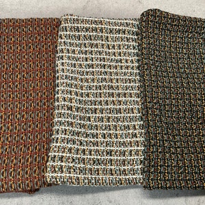 May include: Three fabric swatches with a woven pattern. The swatches are in shades of brown, beige, and black with hints of yellow and blue.