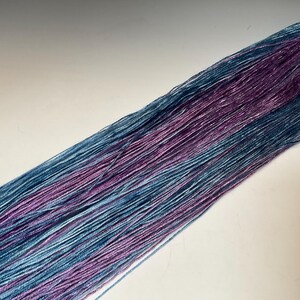 May include: Close-up of a bundle of yarn with a gradient of colors. The yarn transitions from a light blue to a deep purple hue. The yarn is tightly spun and appears soft, ideal for knitting or crocheting projects.