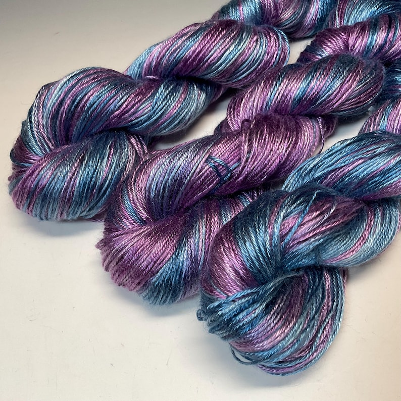 May include: A white ceramic mug with a black handle and the text "But First, Coffee" in a bold, black font. The mug is set against a blurred background, suggesting a cozy setting.