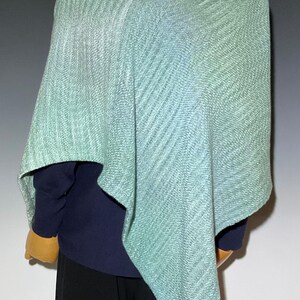 Pu&ograve; includere: Un poncho verde acqua chiaro con un motivo a trama diagonale strutturato. Il poncho &egrave; drappeggiato su un manichino, rivelando una camicia blu navy a maniche lunghe e pantaloni neri. L'indumento ha una vestibilit&agrave; rilassata e una sottile sfumatura di colore.