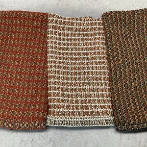 May include: Three kitchen towels with a woven texture. The towels are in shades of brown, green, and white. The towels are lined up side by side.
