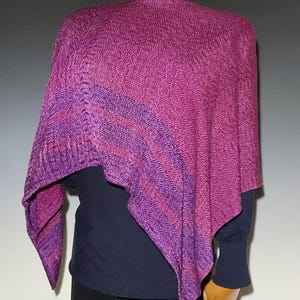 May include: A knitted poncho featuring a vibrant magenta and purple herringbone pattern. The garment has an asymmetrical drape with a textured surface and a deep, saturated color palette that transitions between shades of pink, violet, and purple.
