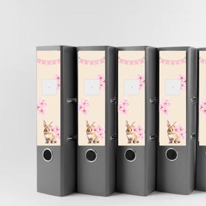 May include: Five grey file folders with a pastel pink and cream design featuring a bunny rabbit and pink flowers. The folders have a ring binder mechanism and a label area on the front.