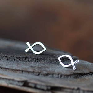 May include: A pair of silver fish symbol earrings on a piece of driftwood.