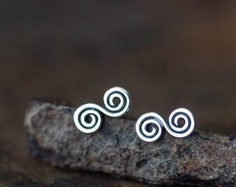 May include: A pair of silver earrings with a double spiral design. The earrings are on a piece of wood.