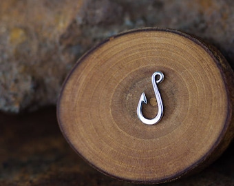 Puede incluir: Un amuleto de anzuelo de pesca plateado sobre un fondo de madera.