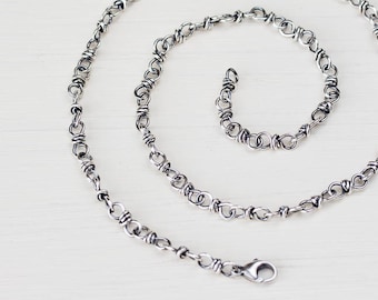 May include: A silver chain necklace with a twisted link design. The chain is laying on a white surface.