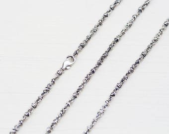 May include: Two silver chains with a delicate, intricate design. The chains are laid out on a white surface.