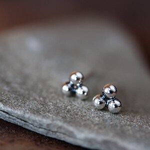 May include: A pair of silver stud earrings with three small, round balls clustered together.