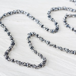 May include: A silver chain necklace with a twisted, barbed wire design.