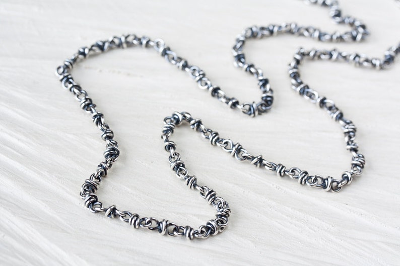 May include: A silver chain necklace with a twisted, barbed wire design.