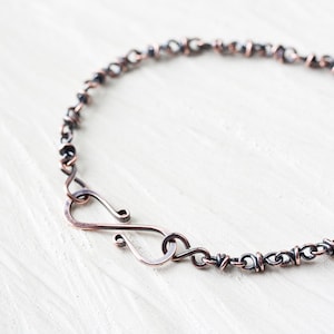 Op de afbeelding: Een koperen en zilveren armband met een gedraaid kettingontwerp en een haakgesp.
