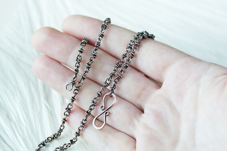 May include: A copper chain necklace with an infinity symbol pendant. The chain is made of two wires twisted together, giving it a unique texture. The necklace is approximately 18 inches long.