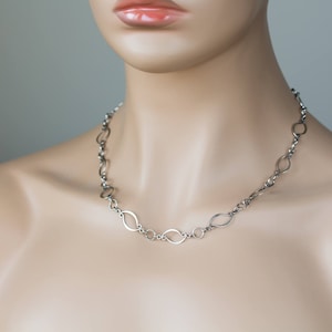 May include: A silver chain necklace with oval-shaped links. The necklace is on a mannequin's neck.