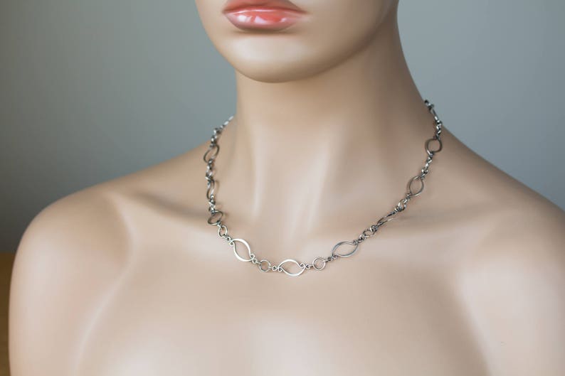 May include: A silver chain necklace with oval-shaped links. The necklace is on a mannequin's neck.