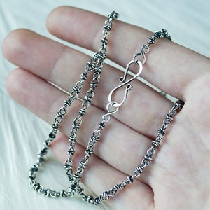 May include: A silver chain necklace with a unique twisted design and a lobster clasp fastening.