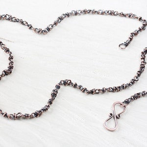 May include: A copper and silver chain necklace with an infinity symbol clasp. The chain is made of small, twisted links.