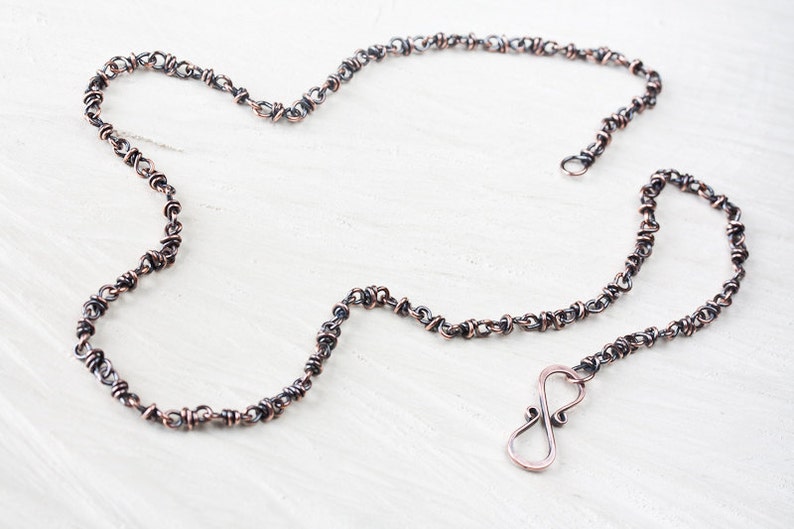 May include: A copper and silver chain necklace with an infinity symbol clasp. The chain is made of small, twisted links.