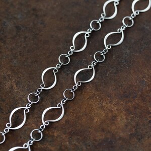 May include: A silver chain necklace with a unique, interlocking, leaf-shaped design. The chain is made of small, delicate links.