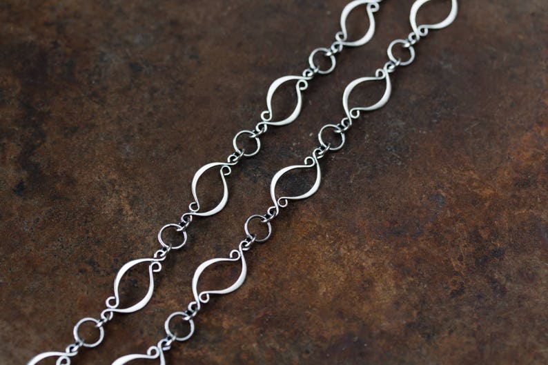 May include: A silver chain necklace with a unique, interlocking, leaf-shaped design. The chain is made of small, delicate links.