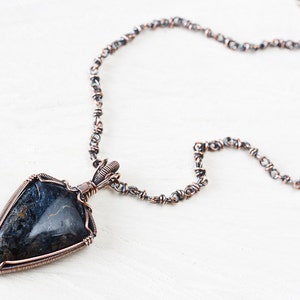 May include: A copper wire wrapped pendant necklace featuring a dark blue and brown gemstone with a silver chain.
