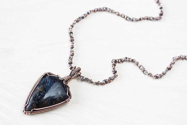 May include: A copper wire wrapped pendant necklace featuring a dark blue and brown gemstone with a silver chain.