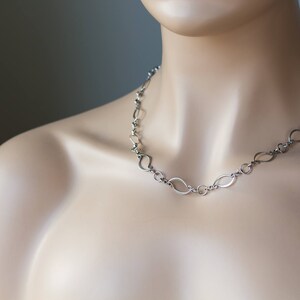 May include: A silver chain necklace with a unique, modern design featuring interconnected oval links.