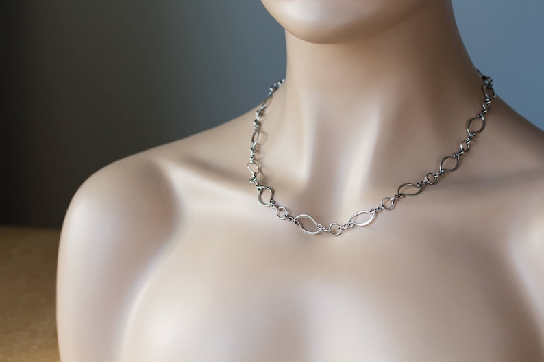 May include: A silver chain necklace with a unique, modern design featuring interconnected oval links.