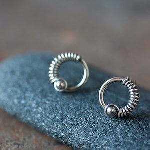 Può includere: Un paio di orecchini d'argento con un design a filo avvolto e una piccola perla nella parte inferiore di ogni orecchino.