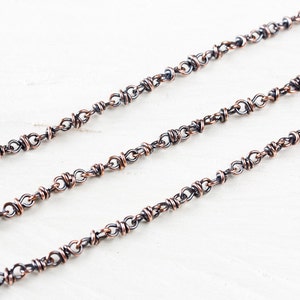 May include: A close-up of a silver chain with copper accents. The chain is made of small, linked rings.