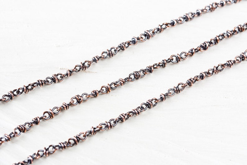 May include: A close-up of a silver chain with copper accents. The chain is made of small, linked rings.