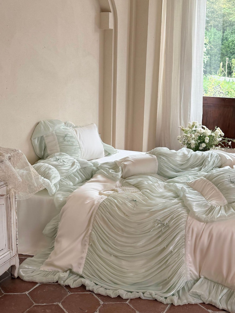 May include: A mint green and white bedding set featuring a ruffled duvet cover with small decorative bows and pearl accents. The set includes matching ruffled pillowcases and a smooth white flat sheet, creating a layered, textured appearance.