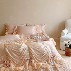 May include: A light pink bedding set featuring a duvet cover with gathered, draped fabric, ruffled edges, and decorative ribbon bows. The set includes matching pillowcases with ruffled borders, creating a layered, textured appearance on the bed.