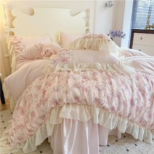 Peut inclure: Un lit avec une parure de lit rose clair à motifs floraux. La housse de couette et les taies d'oreiller ont des bords à volants. Le lit comprend également un jupon rose clair. La tête de lit est blanche.