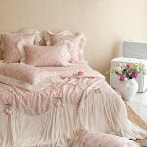 Puede incluir: Un juego de cama de tela rosa suave con un delicado estampado de tulipanes. El edred&oacute;n y las fundas de almohada est&aacute;n adornados con bordes de volantes y detalles de tela plisada en color crema. El conjunto incluye varias almohadas y colcha.
