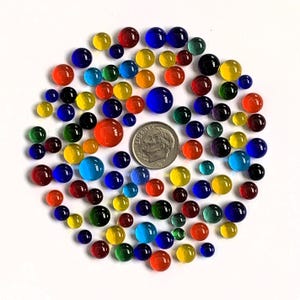 May include: A collection of colorful glass marbles in various sizes and hues, including red, orange, yellow, green, blue, and black. A dime is included for size reference. The marbles are arranged in a circular pattern.