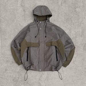 May include: A hooded jacket featuring a vertical pinstripe pattern in shades of brown and grey. The garment includes solid olive-green panels on the chest and sleeves, a front snap-button closure, black zippered pockets, and adjustable drawstrings.