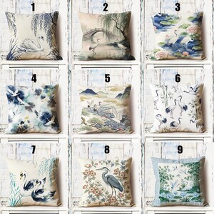 May include: Nine decorative throw pillows with various Asian-inspired designs. The pillows feature images of swans, cranes, bridges, and landscapes in shades of blue, green, and beige. The pillows are square-shaped and made of a textured fabric.