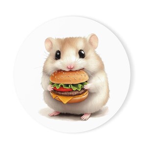 May include: A small, white hamster with brown eyes is holding a hamburger in its paws. The hamster is looking at the camera with a cute expression.