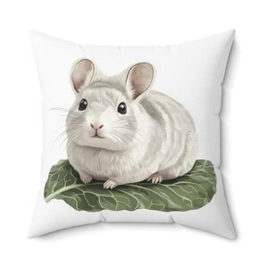 Puede incluir: Cojín cuadrado con una ilustración de acuarela de una chinchilla. La chinchilla es blanca y gris, sentada sobre una gran hoja verde. El cojín tiene un fondo blanco y probablemente está hecho de una tela suave.