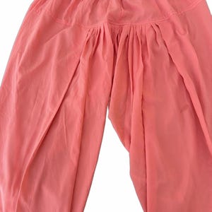 May include: Coral-colored pants with a gathered waist and loose, flowing legs. The fabric appears lightweight and slightly sheer, suggesting a comfortable, casual style. The pants are designed with a relaxed fit, suitable for warm weather or leisure activities.