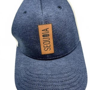 May include: A blue denim baseball cap with a white mesh back. The cap features a brown leather patch with the word "SEQUOIA" in vertical white letters. The cap has a curved brim and a button on top.