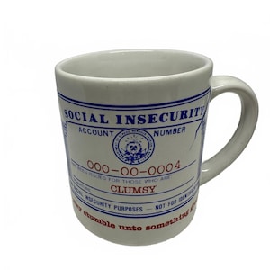 Könnte beinhalten: Ein weißer Keramikbecher mit blauem und rotem Aufdruck. Das Design ähnelt einem offiziellen Dokument mit dem Titel SOCIAL INSECURITY, der Kontonummer 000-00-0004 und dem in roter Tinte gedruckten Wort CLUMSY.