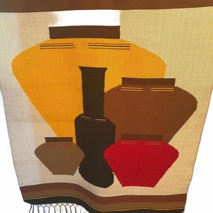 May include: Woven textile featuring stylized pottery in shades of yellow, brown, and red against a beige background. The design includes various pot shapes with horizontal stripe details. The bottom edge has a fringe.